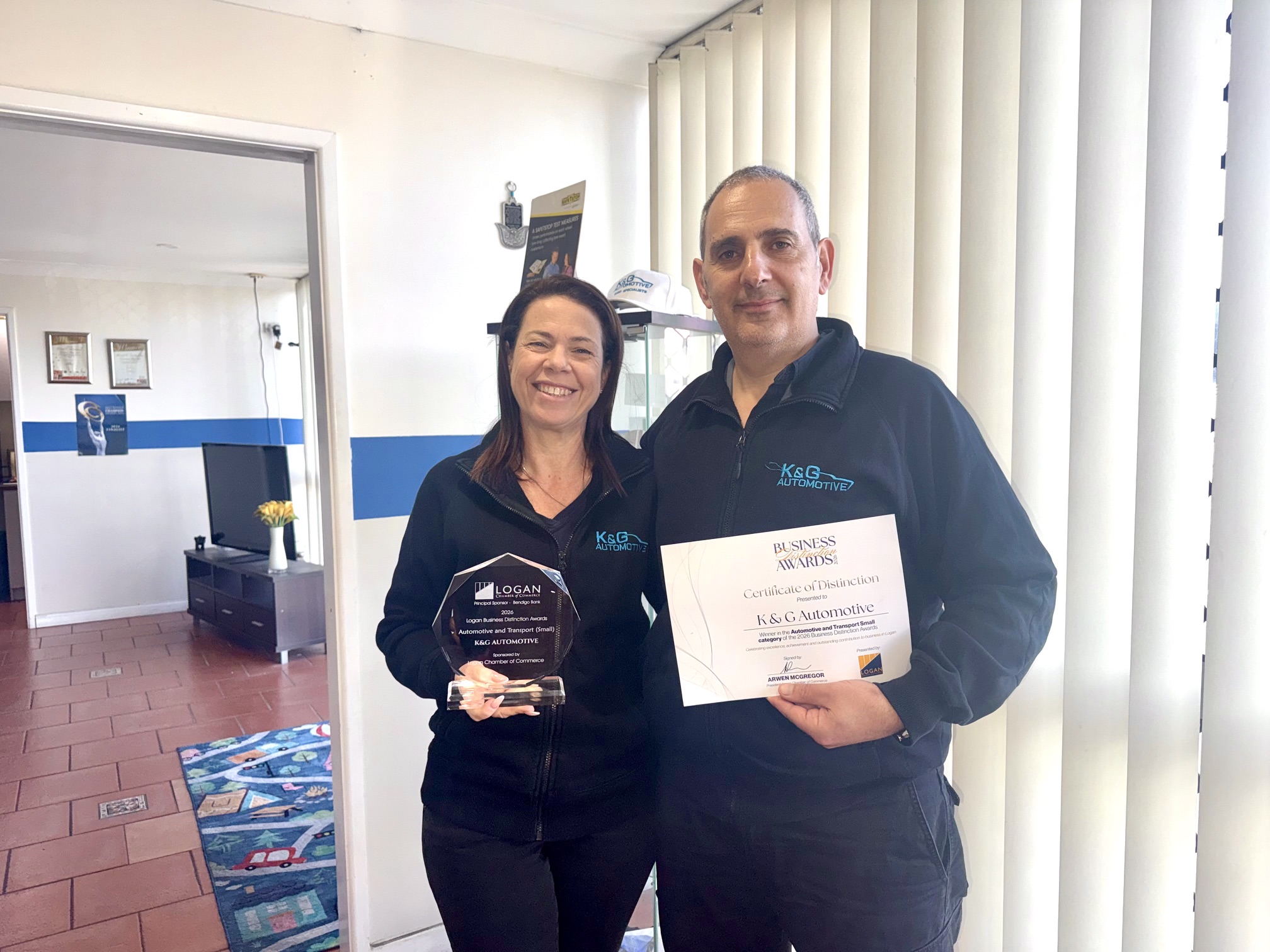 Einat and Shlomi Kuba holding the 2026 Logan Business Distinction Awards trophy and Certificate of Distinction for the Automotive and Transport Small category at K&G Automotive in Underwood